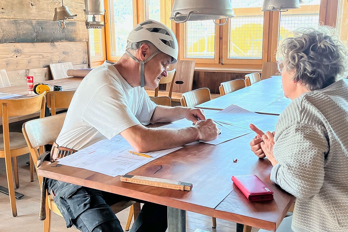 Noldi und Nicole Schindler sitzen an einem Holztisch und schauen sich Pläne an